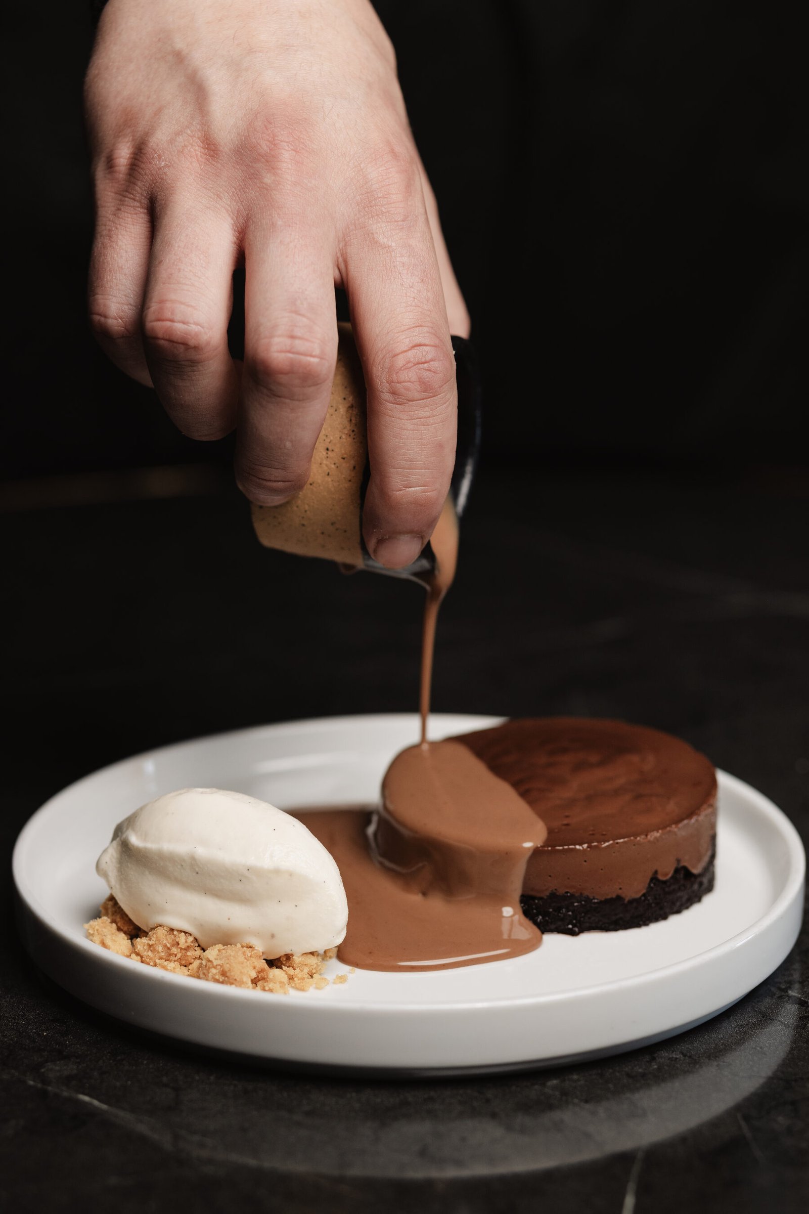 Warm chocolate sauce poured over a chocolate tart with vanilla ice cream